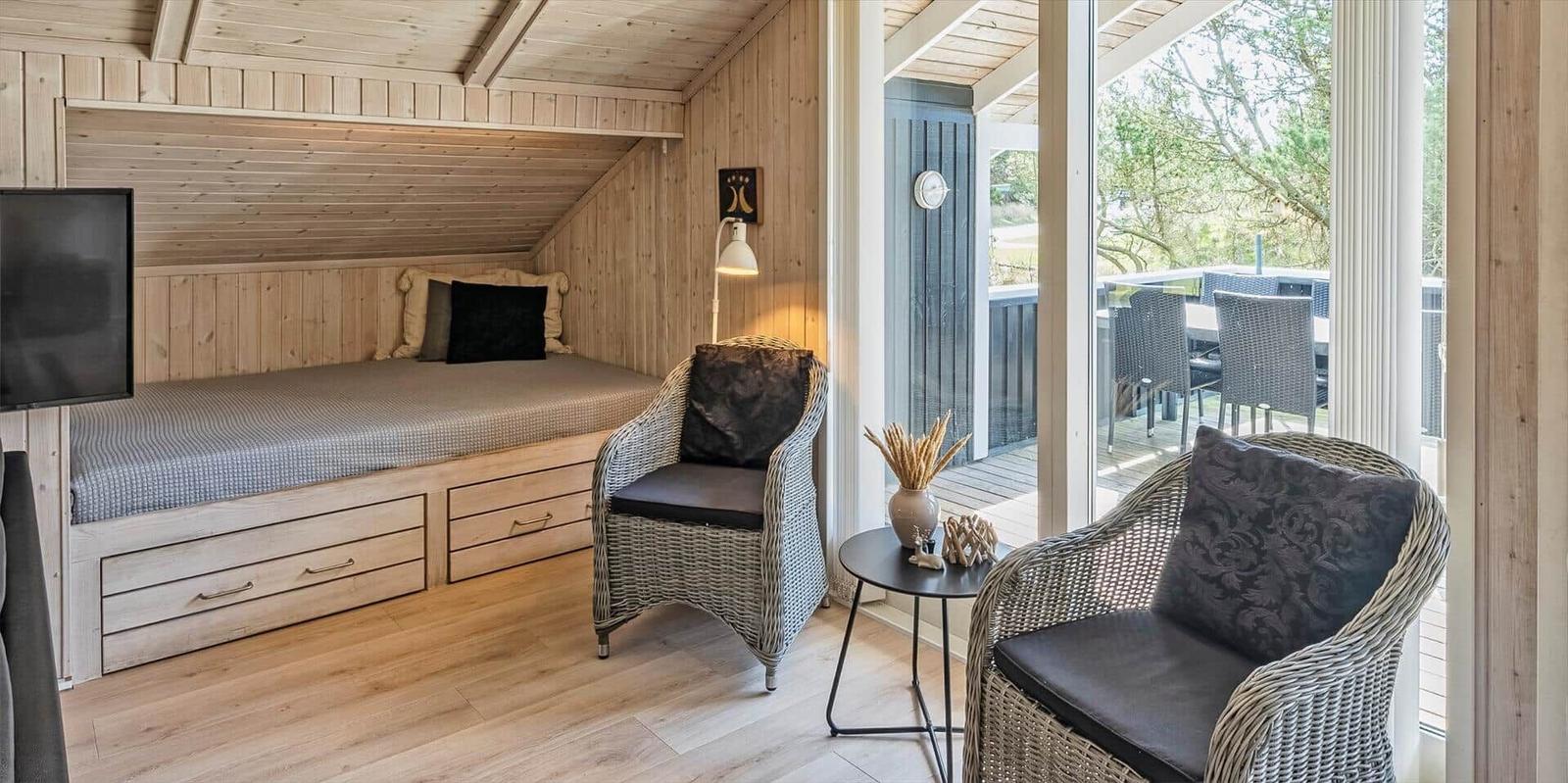 Schlafzimmer mit Doppelbett, zwei Sessel und Blick auf Terrasse.