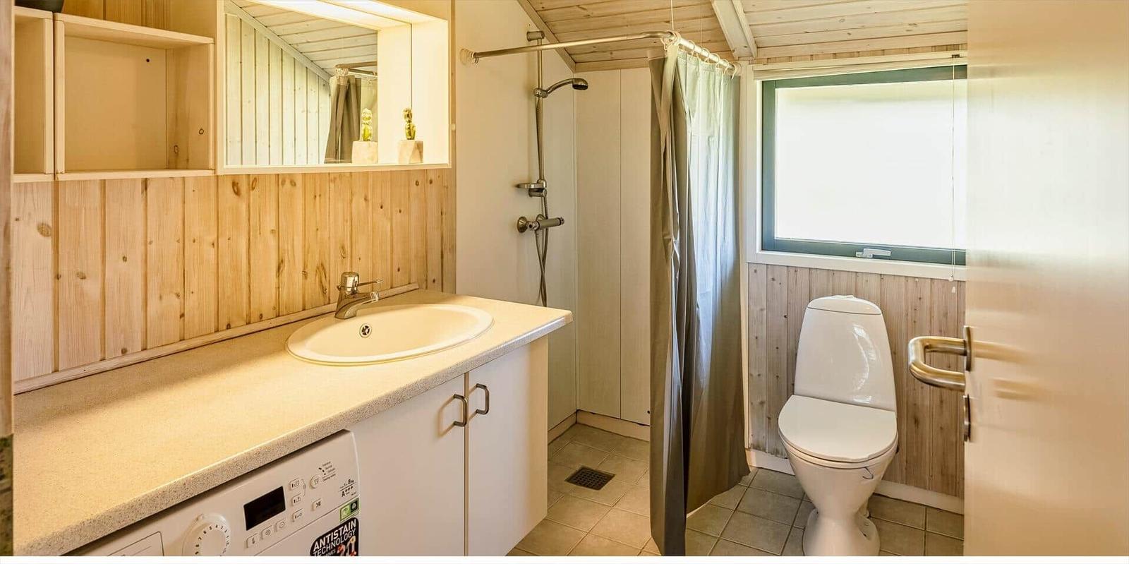 Badezimmer mit Dusche, Toilette und Waschbecken unter Holzwand