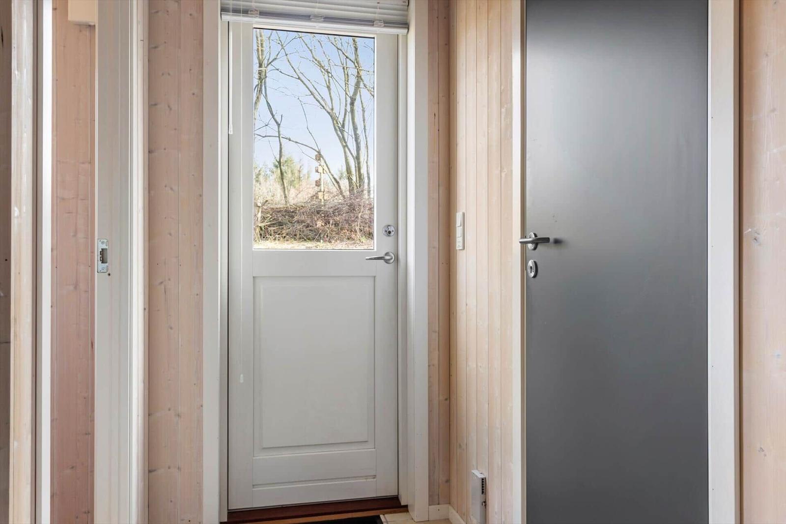 Haus mit weißen und grauen Türen, Holzwand und Fensterblick auf Bäume.