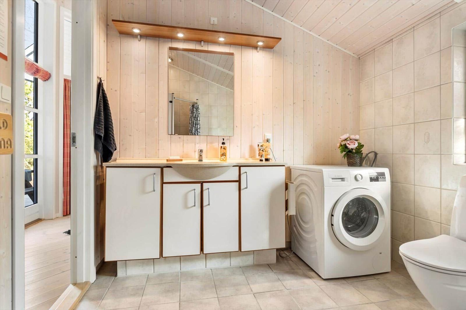 Badezimmer mit Waschmaschine, Waschbecken und Toilette. Holzwand und Fliesenboden.