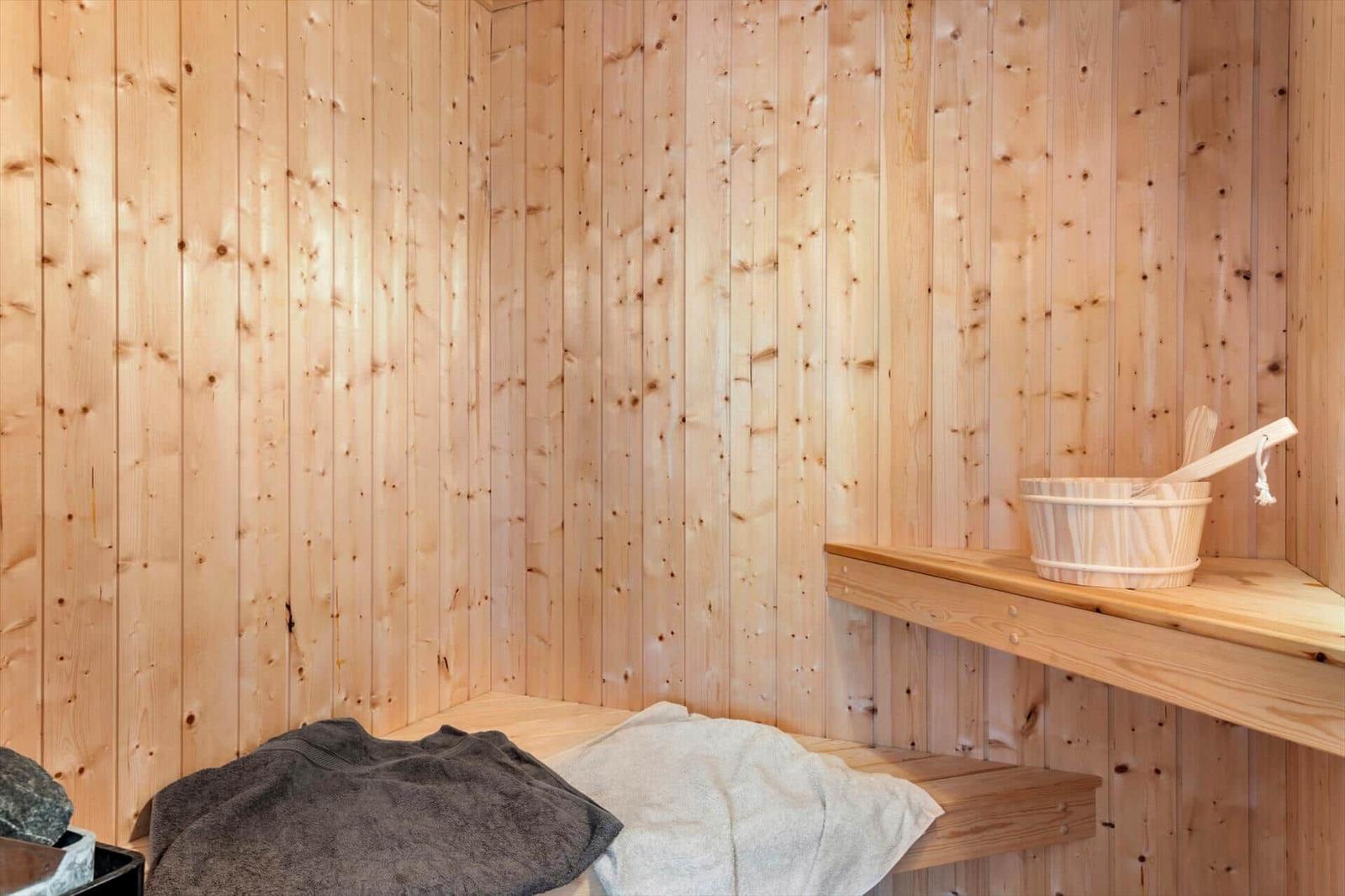 Sauna mit Holzwand, Sitzbank und Holzschale mit Besen.