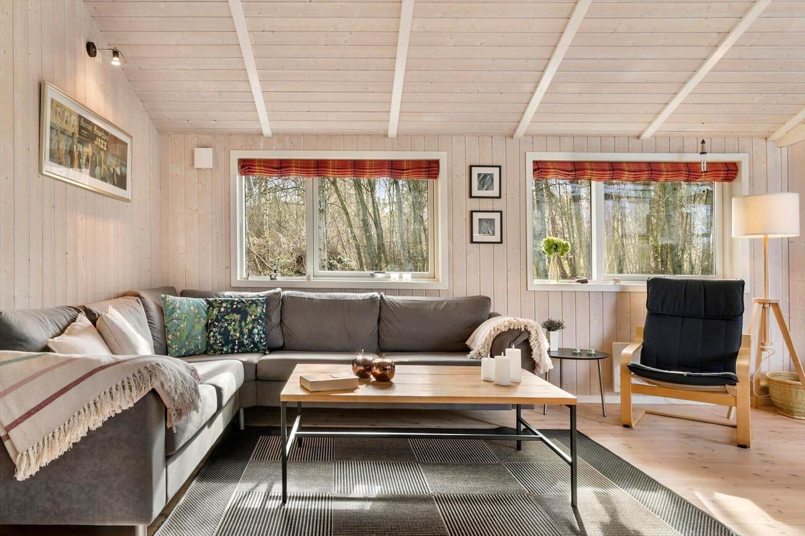 Wohnzimmer mit Sofa, Couchtisch und Sessel. Fenster mit Blick in den Wald.