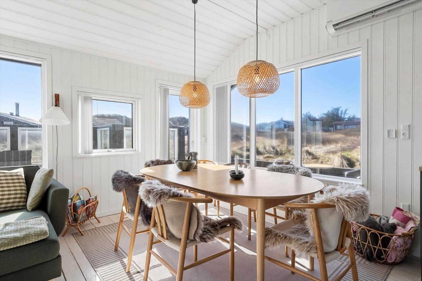 Esszimmer mit Holztisch, Stühlen mit Fell und großen Fenstern.