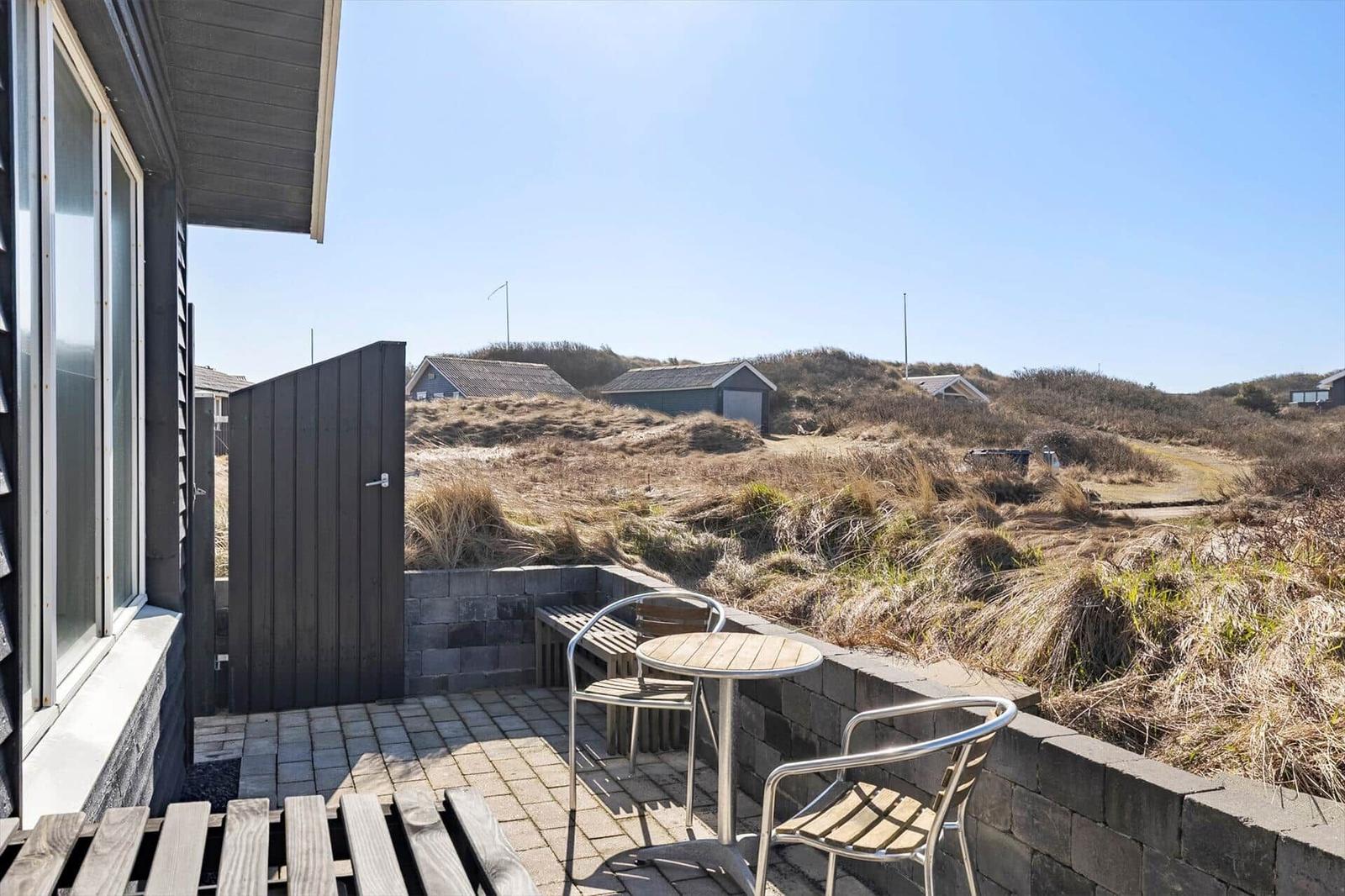 Terrasse mit Tisch und Stühlen, Blick auf Dünen und Häuser.