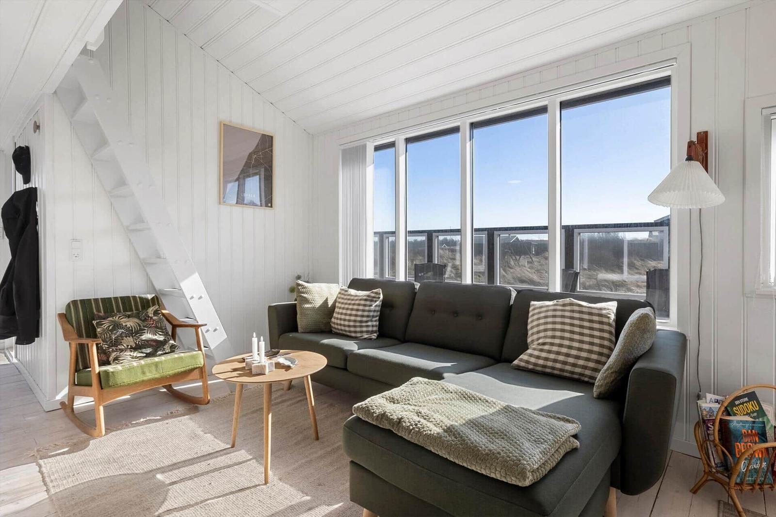 Wohnzimmer mit Sofa, Sessel und großem Fenster. Helle Wände und Holzboden.
