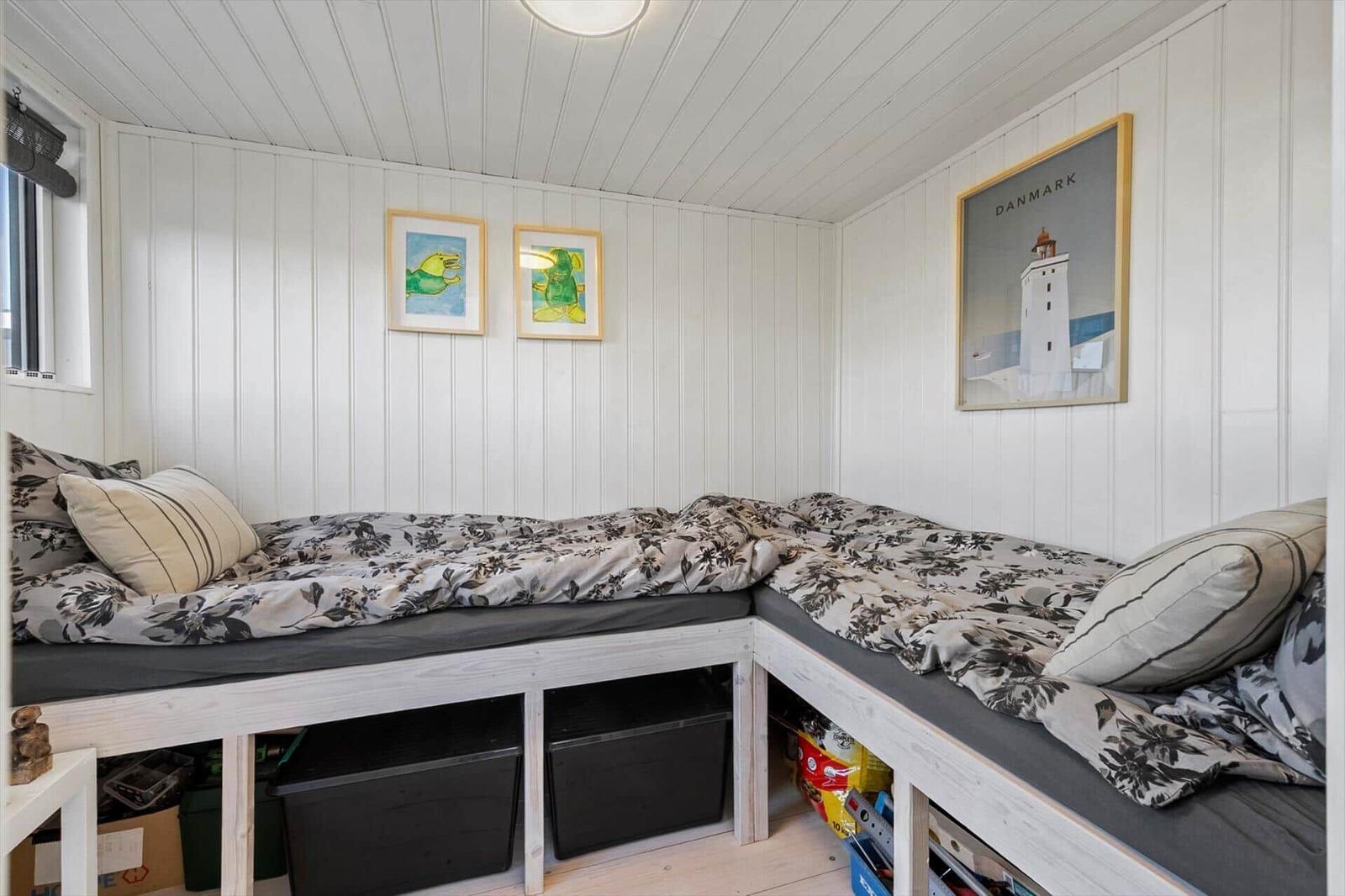 Zimmer mit L-förmigem Bett und Wandbildern an weißen Wänden.
