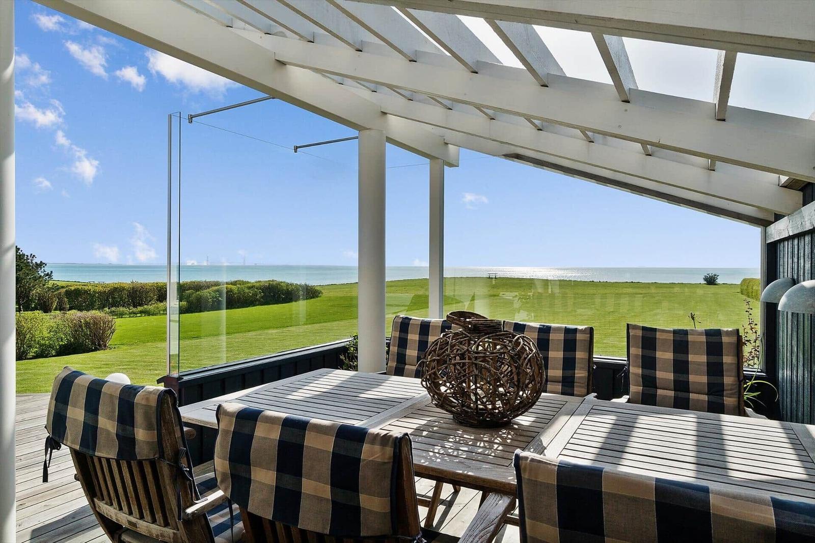 Terrasse mit Tisch und Stühlen unter weißem Dach. Blick auf Grasland und Meer.