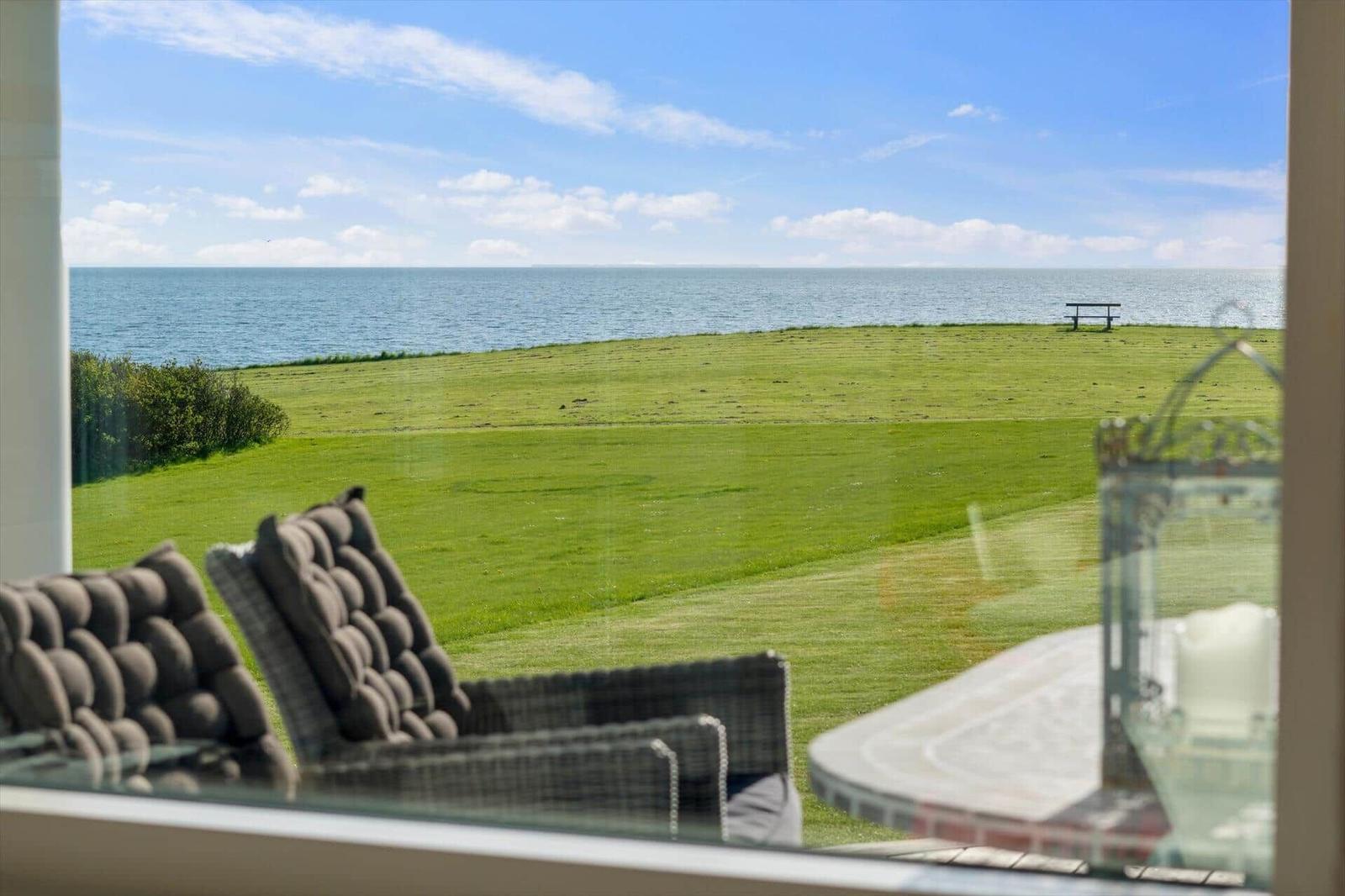 Aus dem Fenster blickt man auf einen grünen Rasen und das Meer.
