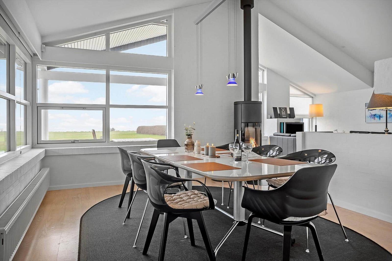 Essbereich mit Tisch, Stühlen und Kamin. Große Fenster mit Blick auf Feld.