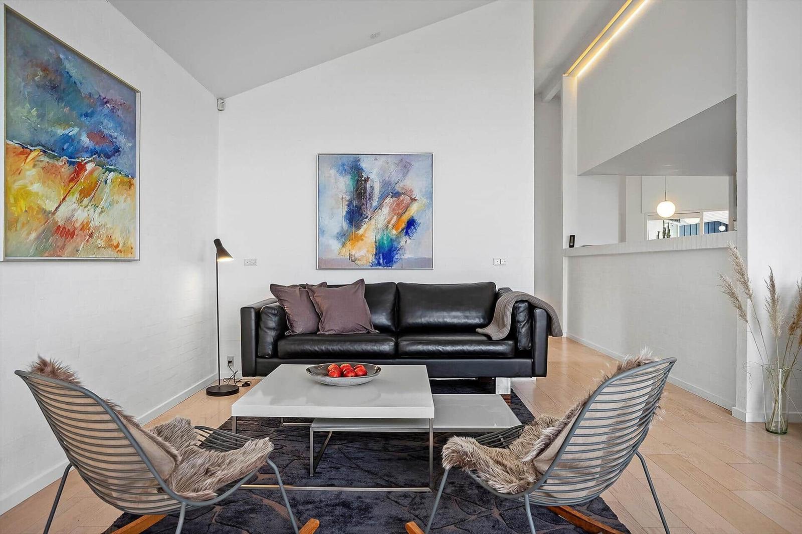 Wohnzimmer mit schwarzer Couch, zwei Stühlen und abstrakten Bildern an den Wänden.