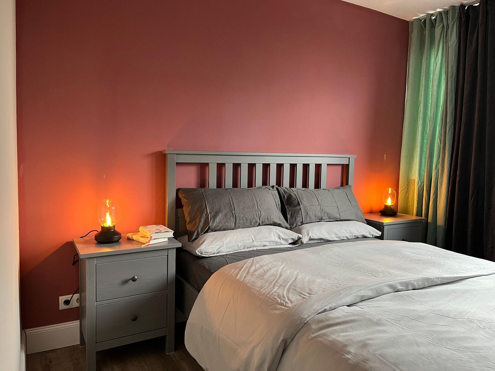 Schlafzimmer mit Bett, Nachttischen und warmen Lampen an der Wand.
