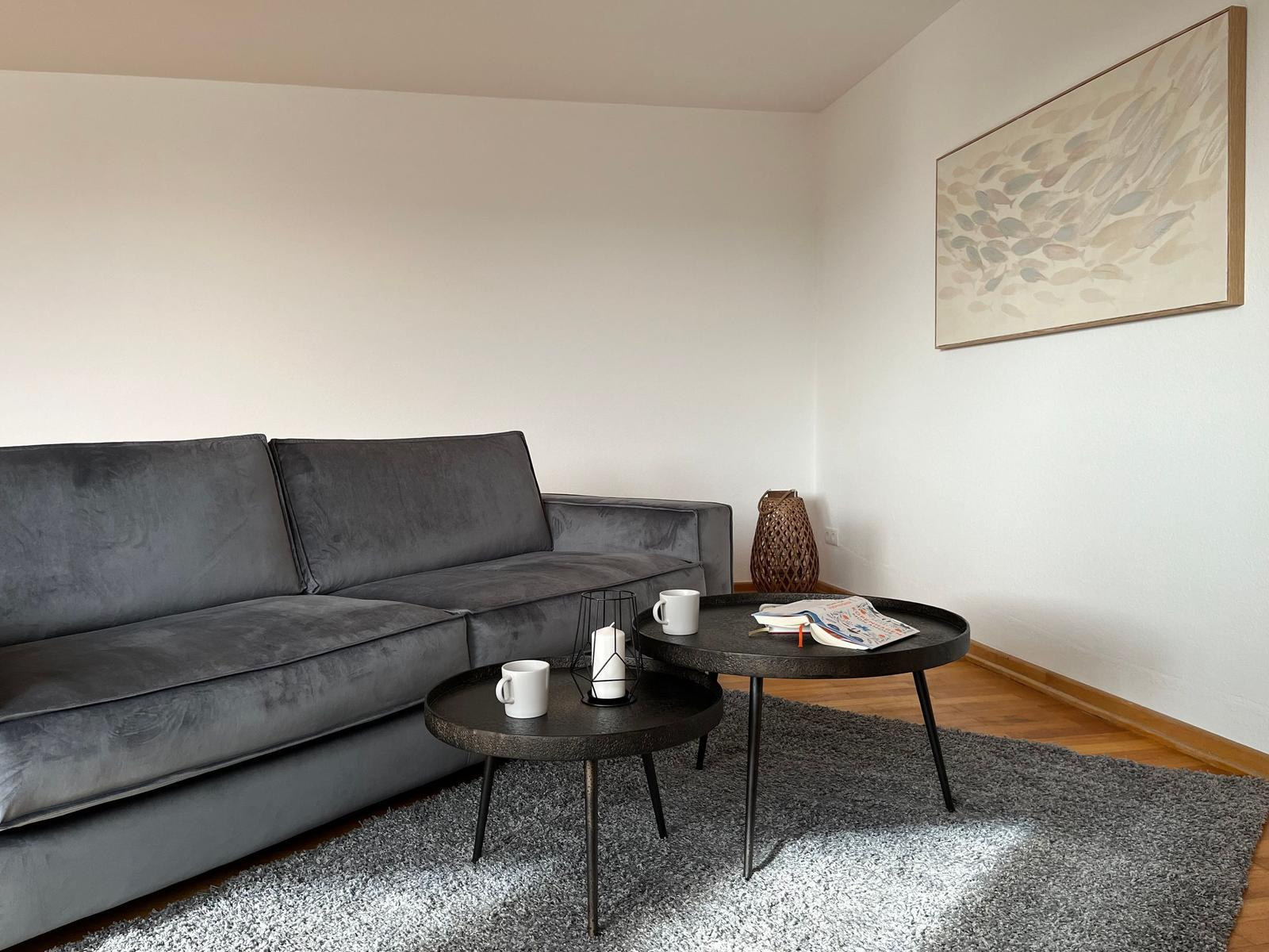 Ein grauer Sofa mit zwei runden Tischen auf einem Teppich