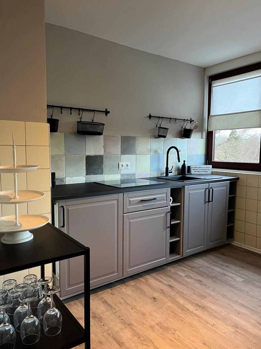 Küche mit Arbeitsplatte, Spüle und Fenster. Holzdielenboden und Wandfliesen.