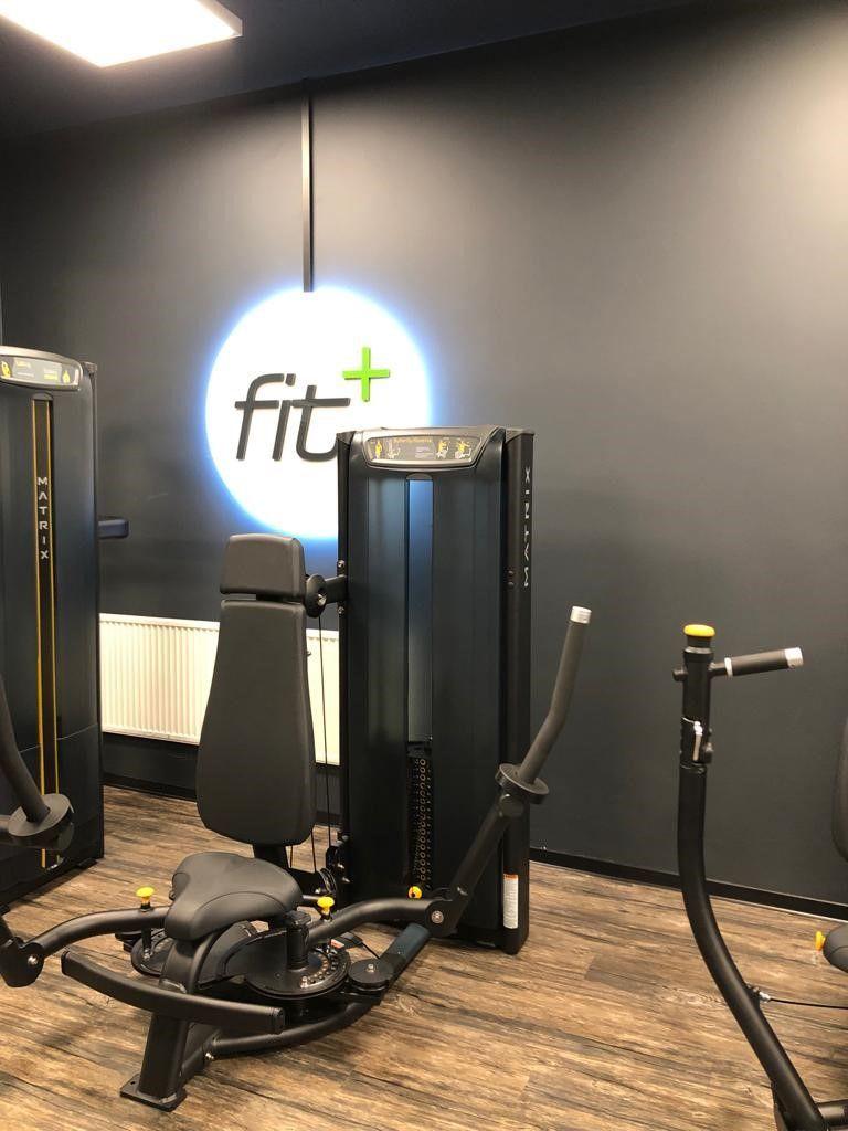 Fitnessraum mit Matrix-Geräten und beleuchtetem Logo an der Wand.