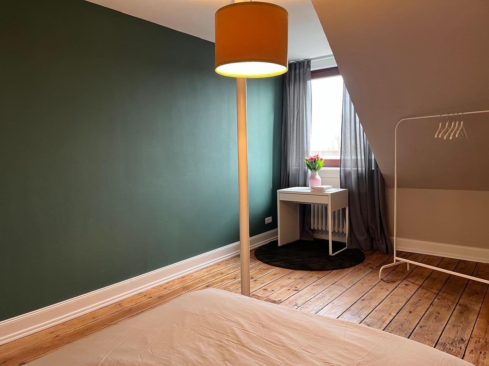 Schlafzimmer mit grünem Wandbereich, Holzboden und Stehlampe.