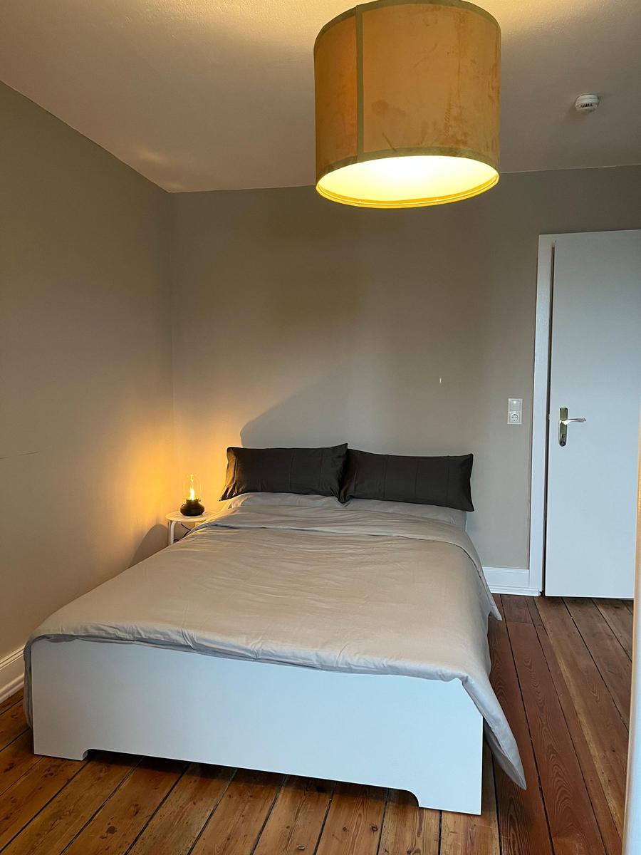 Schlafzimmer mit Bett, Nachttisch, Lampe und Holzboden.