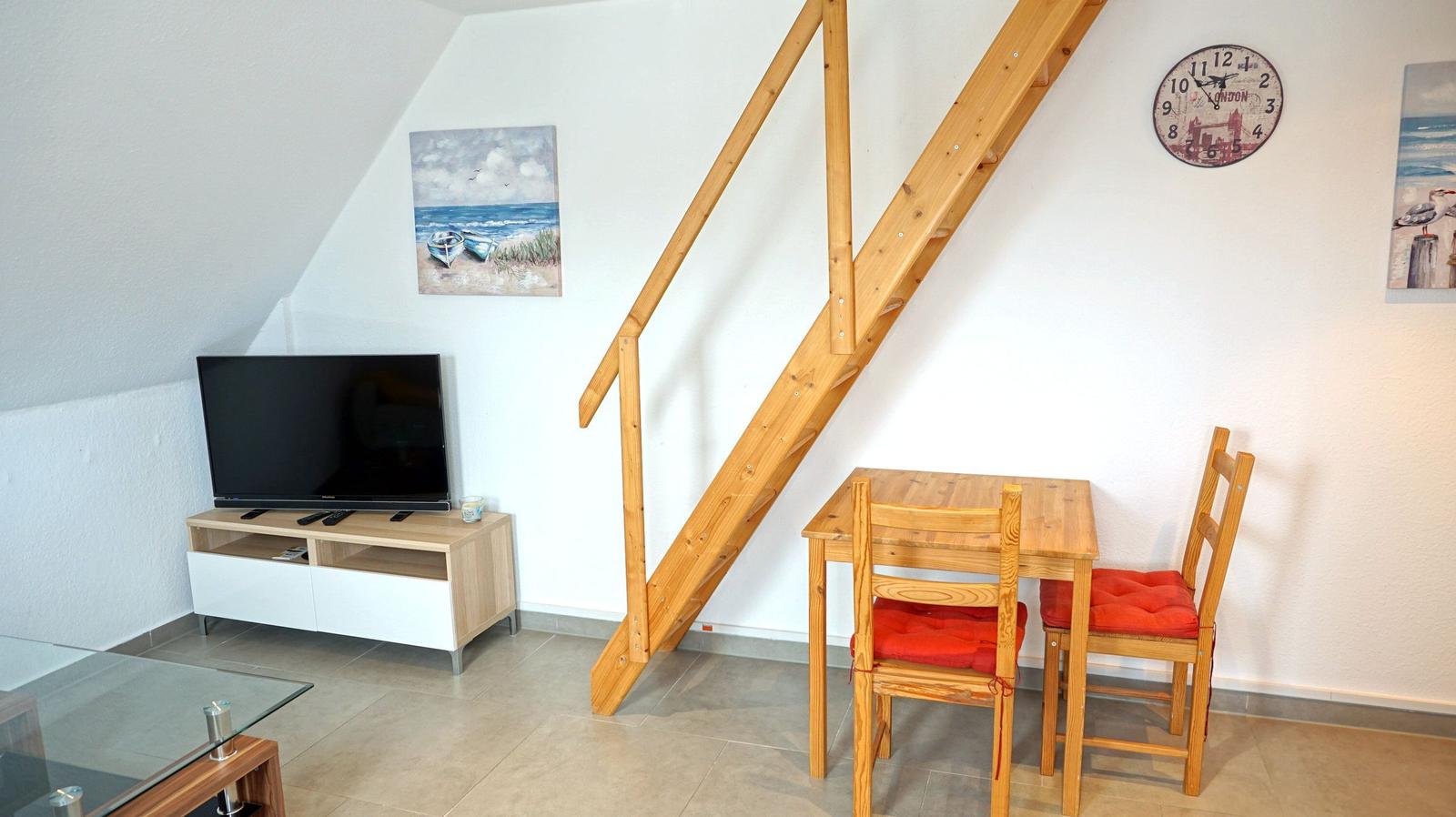 Wohnzimmer mit TV, Esstisch und Holztreppe zur oberen Etage.