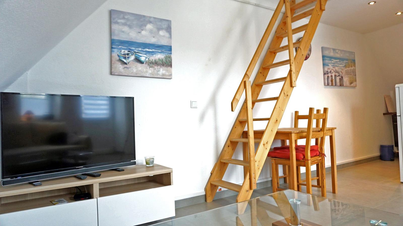 Wohnzimmer mit TV, Essbereich und Holztreppe zur oberen Etage.