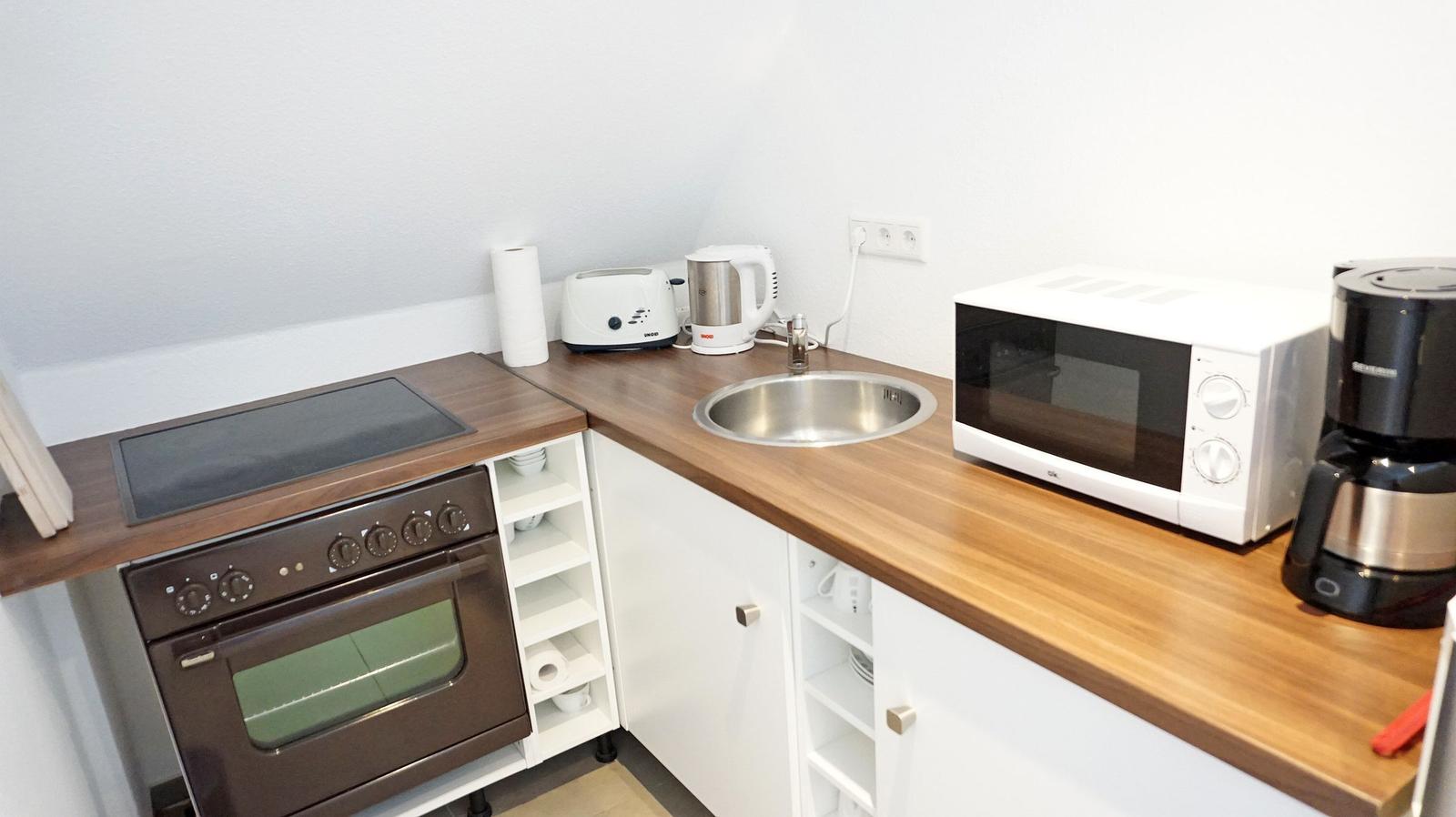 Küche mit Herd, Spüle, Mikrowelle und Kaffeemaschine.