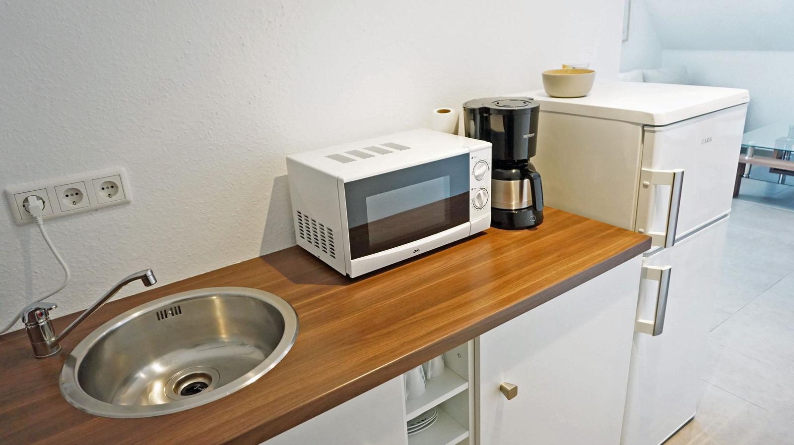 Küchenzeile mit Spüle, Mikrowelle, Kaffeemaschine und Kühlschrank.