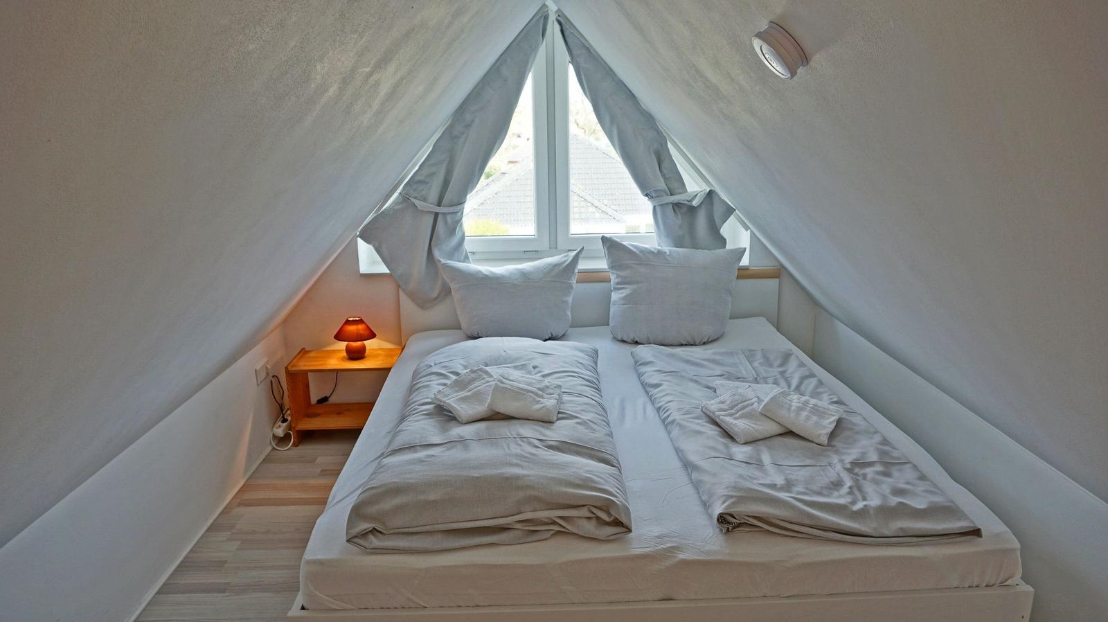 Doppelbett unter Dachschrägen mit Fenster und Nachttisch.