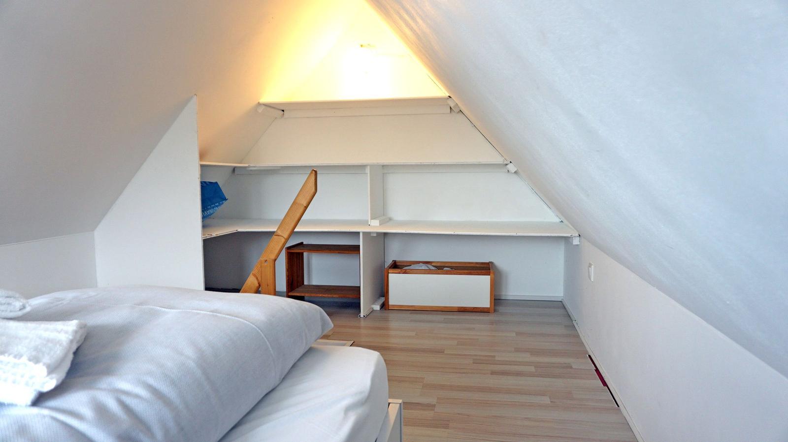Schlafzimmer mit Dachschräge, Bett und Regalsystem.
