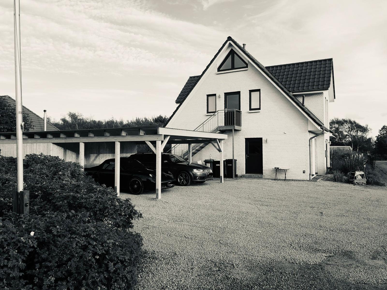 Haus mit Carport, zwei Autos und Garten. Eingangstür und Balkon sichtbar.