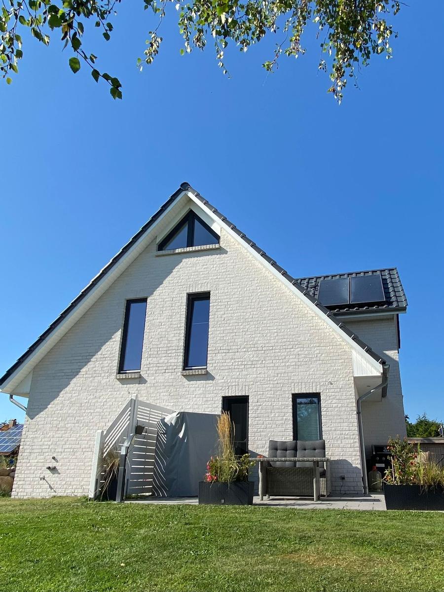 Modernes Haus mit weißen Wänden und großem Garten unter blauem Himmel.