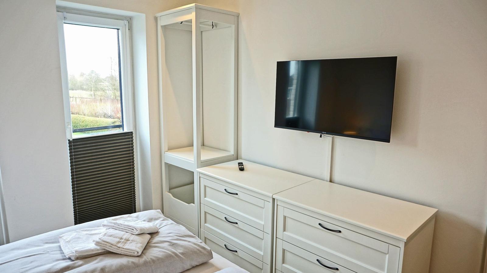 Schlafzimmer mit Bett, Schrank, TV und Fenster.