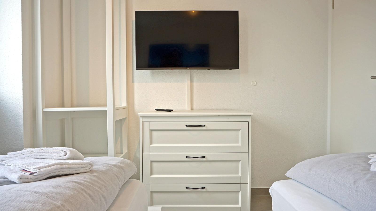 Zimmer mit zwei Betten, Schrank und Wandfernseher.