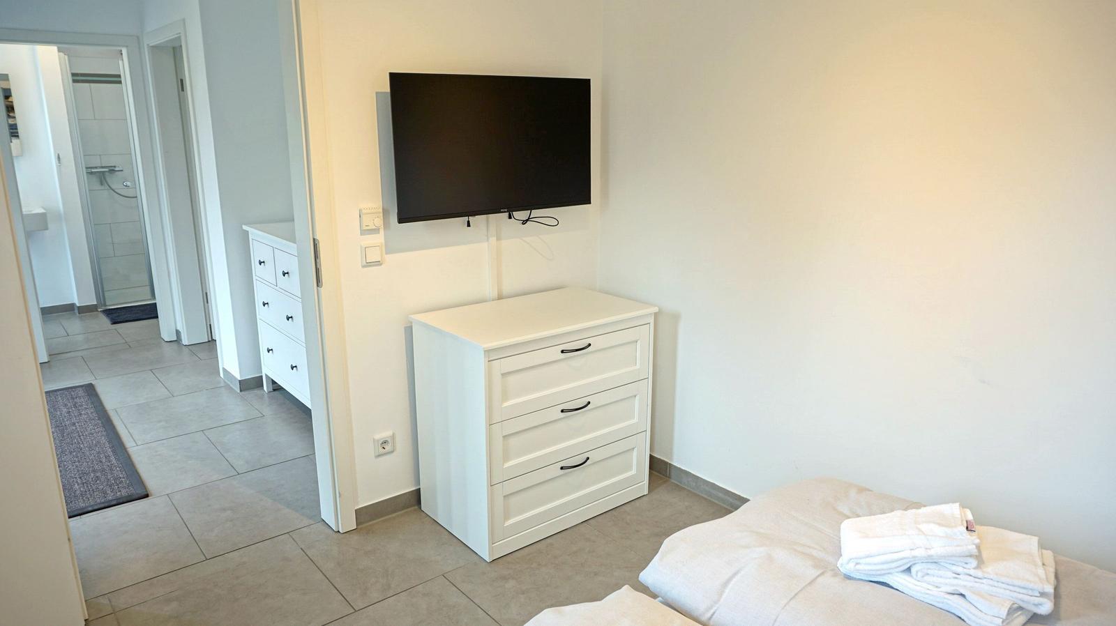 Schlafzimmer mit Bett, Schrank und Wand-TV. Blick in das Bad.