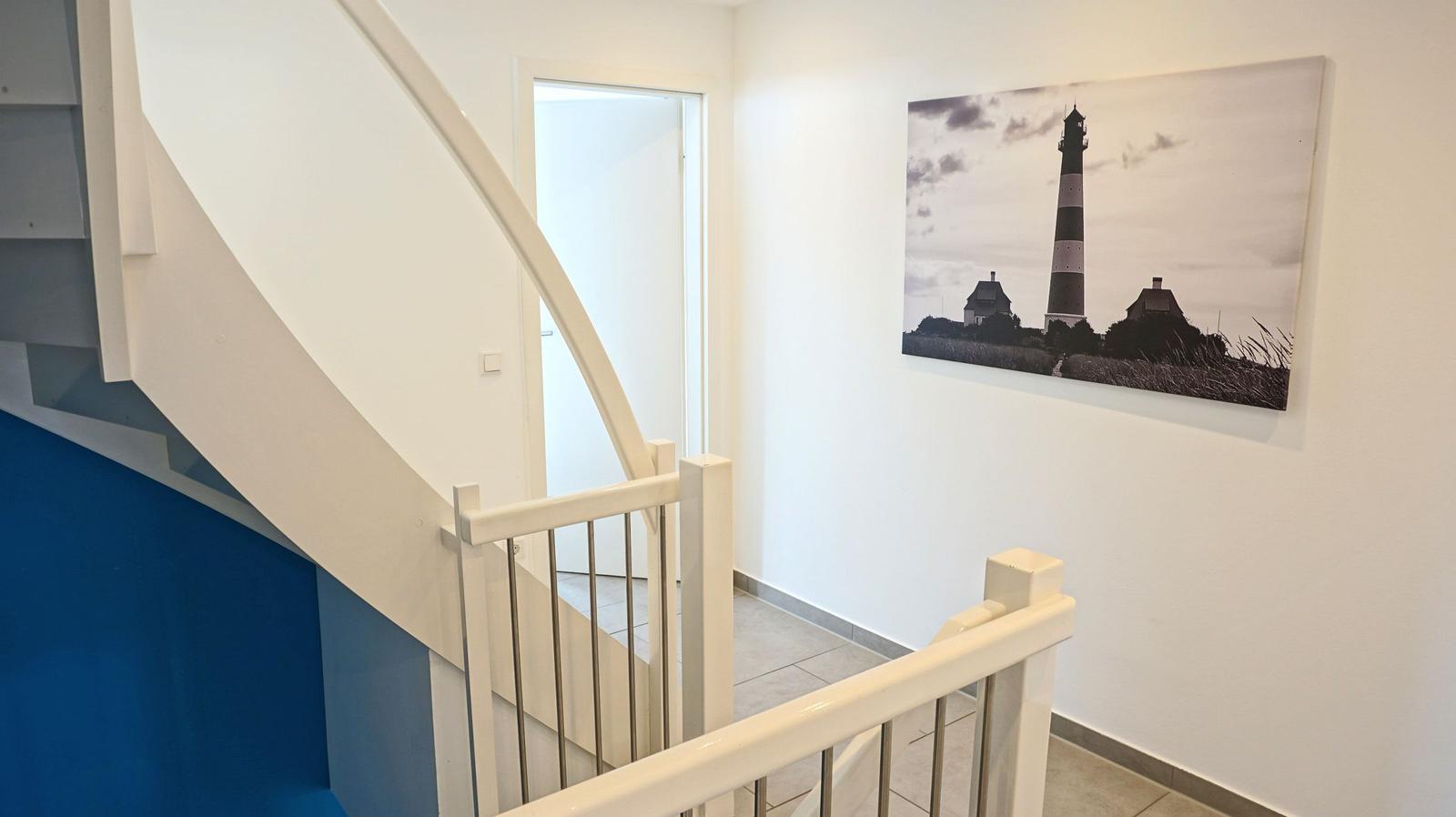 Treppenhaus mit Wandbild eines Leuchtturms und weißer Geländer.