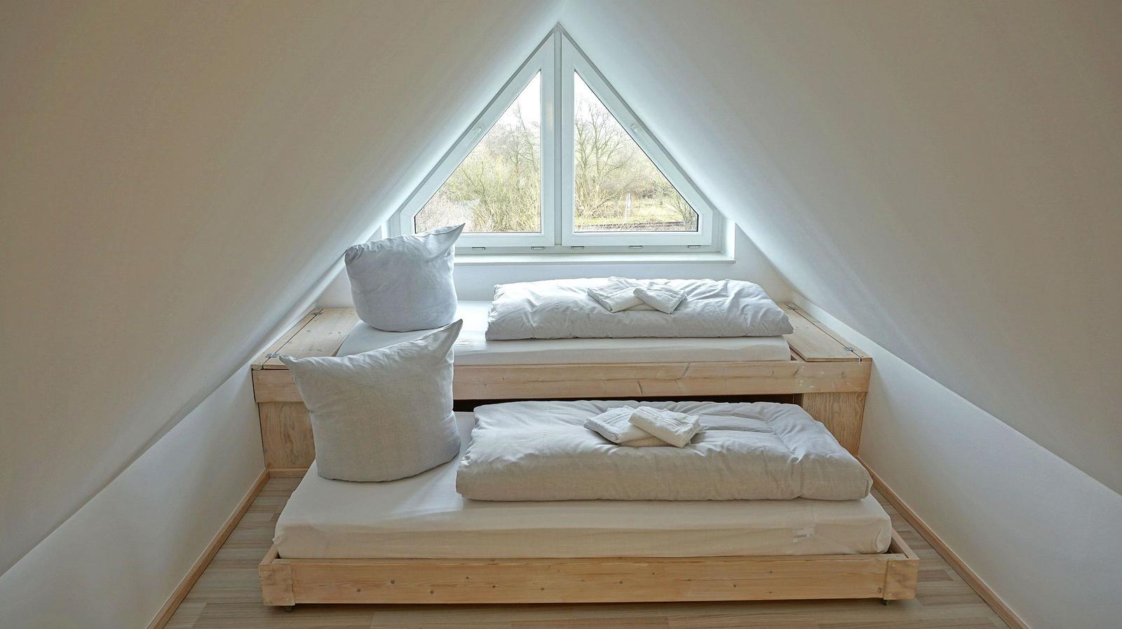 Zwei Matratzen auf Holzrahmen unter Dachschrägen mit Fenster