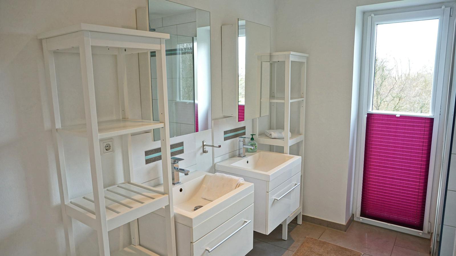 Badezimmer mit zwei Waschbecken, Spiegeln und Fenster mit pinken Jalousien.