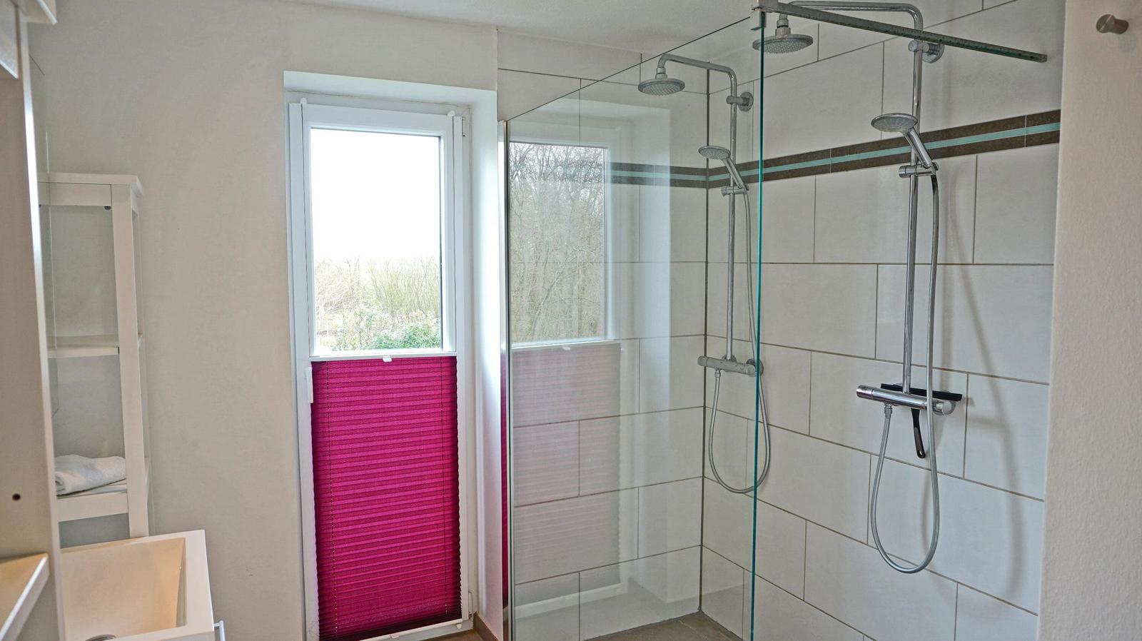 Badezimmer mit Dusche und Fenster mit rosa Jalousie.
