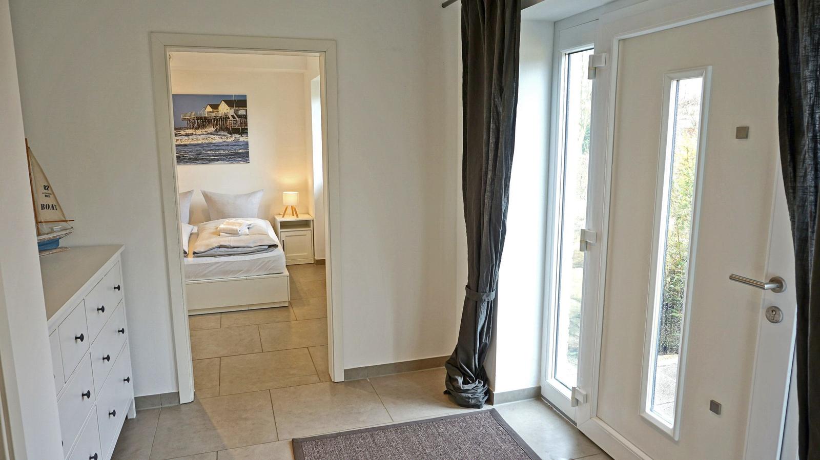 Schlafzimmer mit Bett und Wandbild. Tür führt nach draußen.