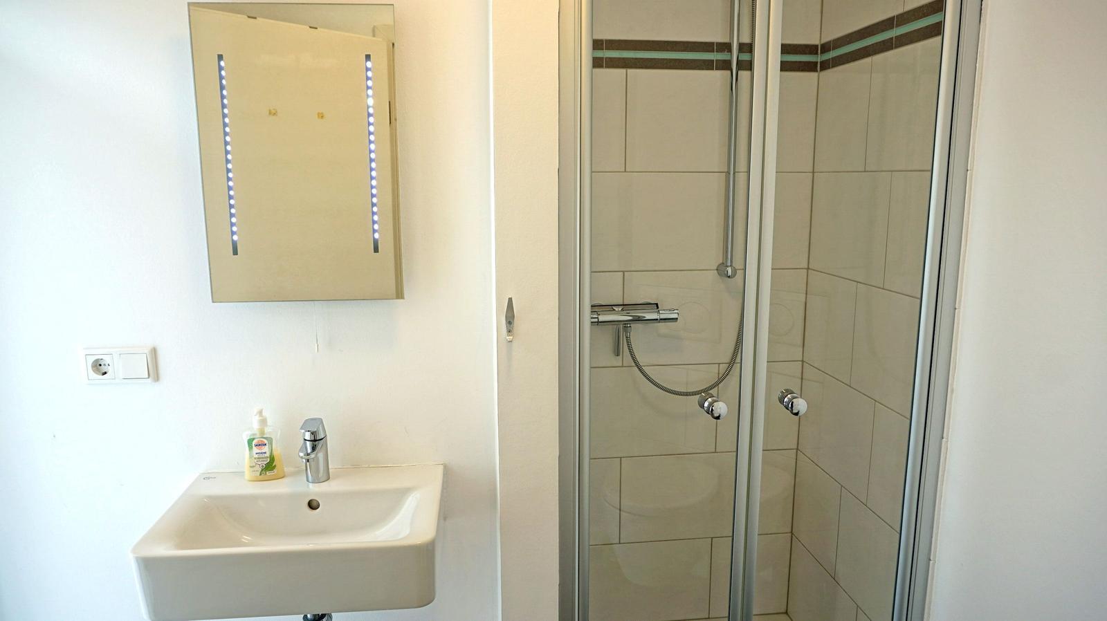 Badezimmer mit Dusche und Spiegelschrank mit LED-Beleuchtung.