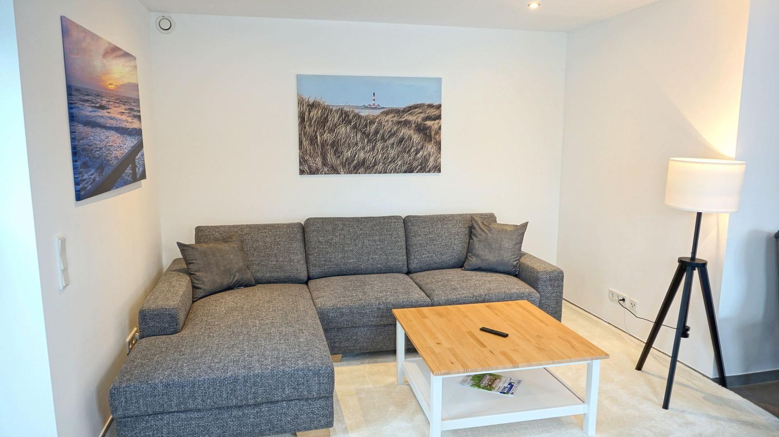 Wohnzimmer mit grauem Sofa, Holztisch und Wandbildern.