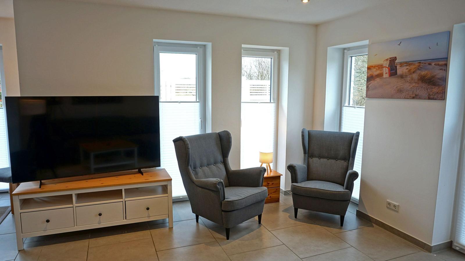 Wohnzimmer mit zwei Sesseln, Fernseher und Fenstern.