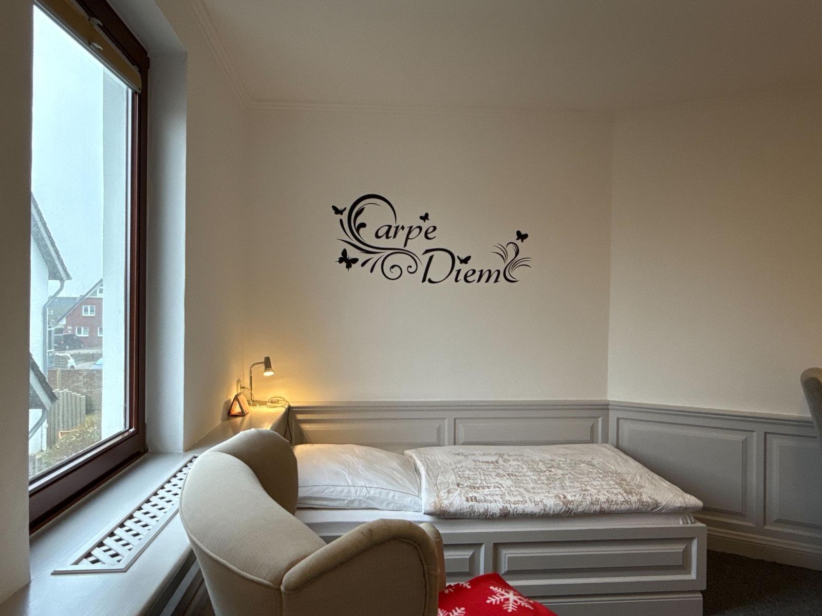 Bedroom with bed, window, and wall decoration Carpe Diem.