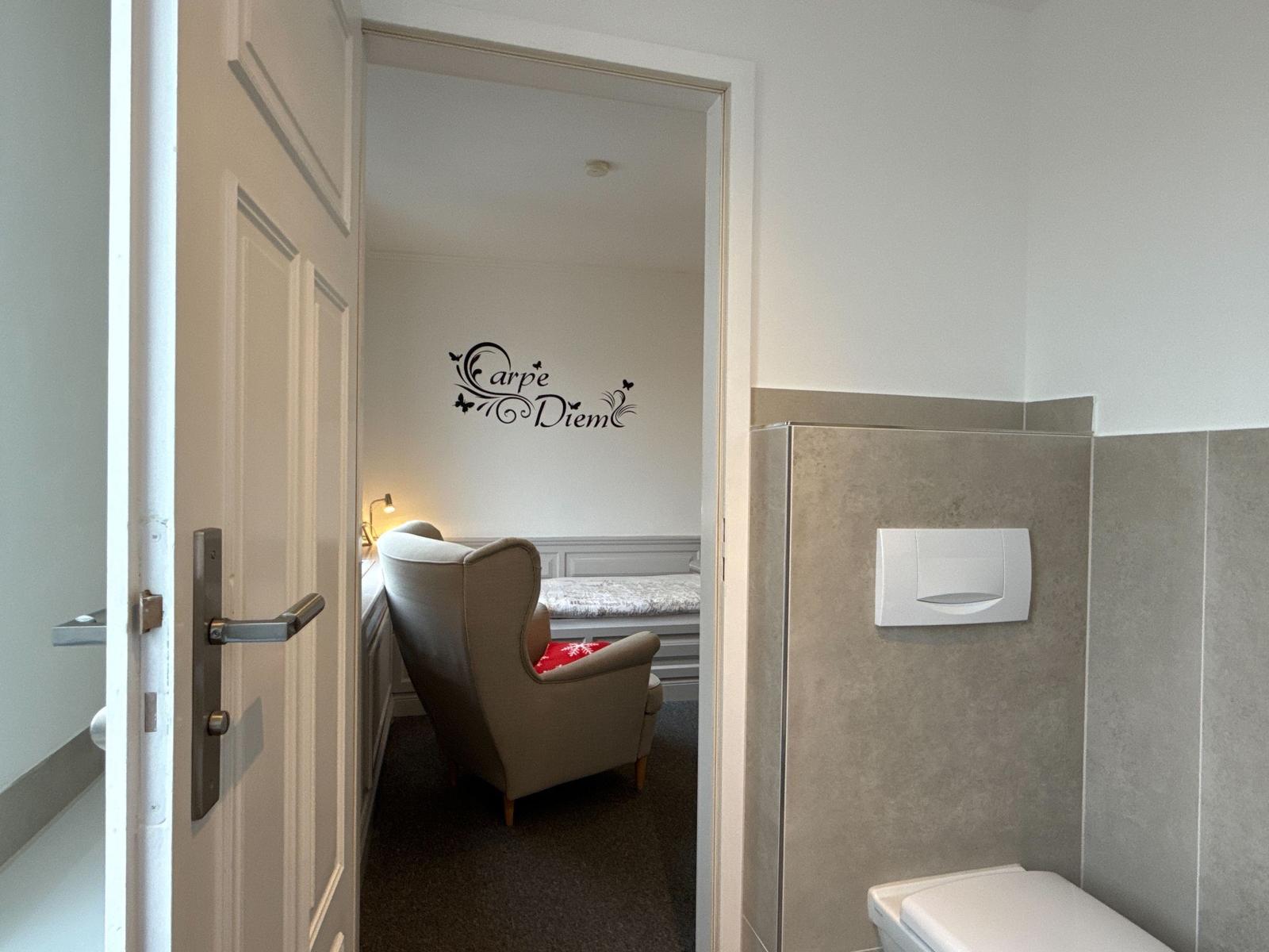 A room with chair and wall decoration. Toilet area to the right.