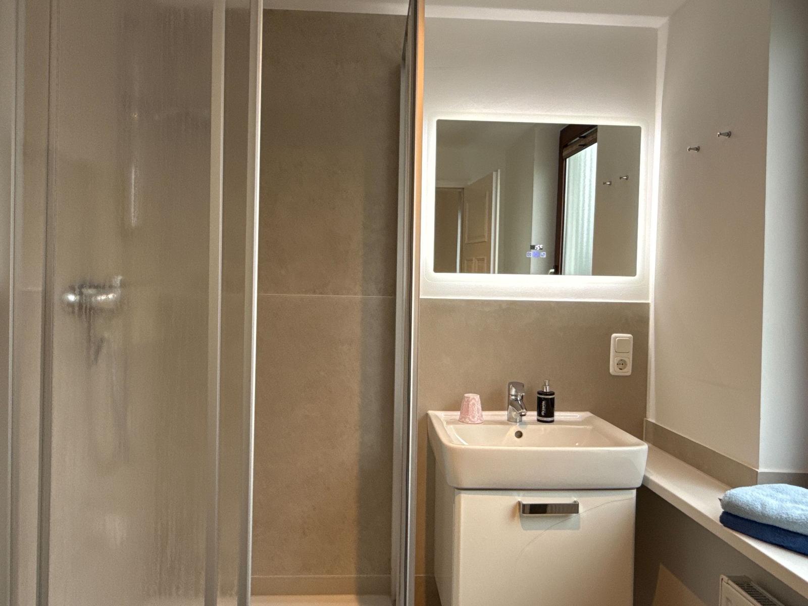 Bathroom with shower, sink, and lit mirror.