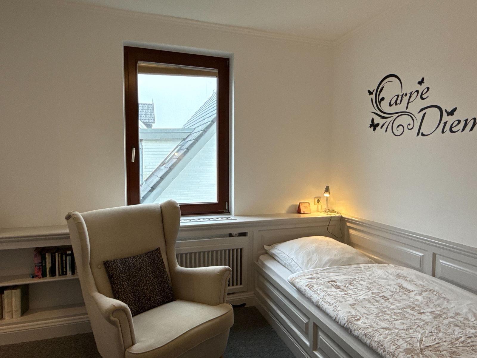 Bedroom with bed, armchair, and wall decoration.