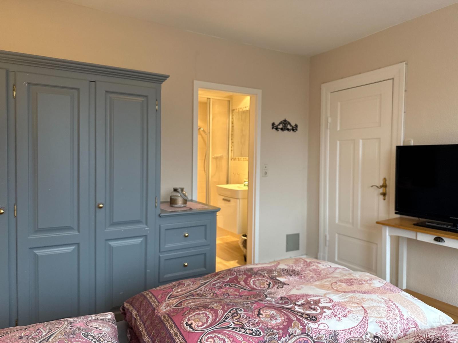 Schlafzimmer mit Bett, Kleiderschrank und TV. Badezimmer ist angrenzend.