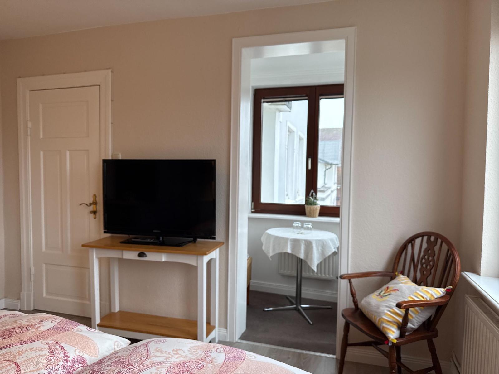 Schlafzimmer mit TV, Stuhl und Blick auf Balkon.