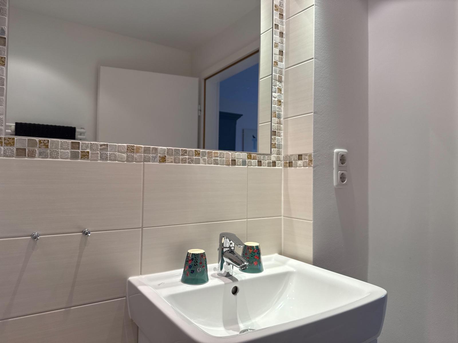 Waschbecken mit Spiegel und Mosaikfliesen an der Wand.