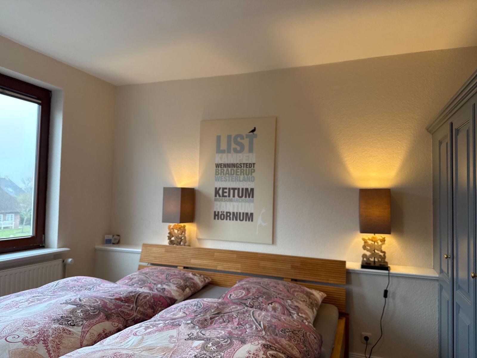 Schlafzimmer mit Bett, Wandbild und zwei Nachttischen mit Lampen.