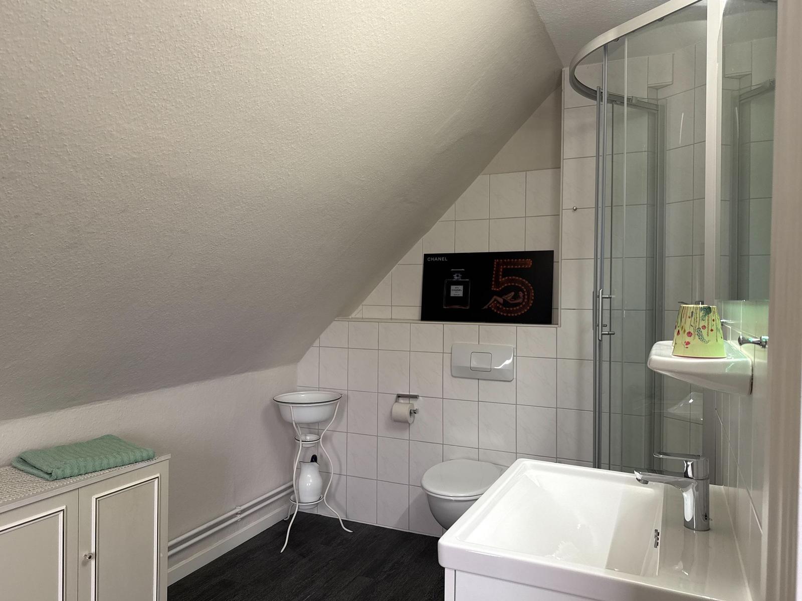 Bathroom with shower, sink, and toilet under sloped ceiling.