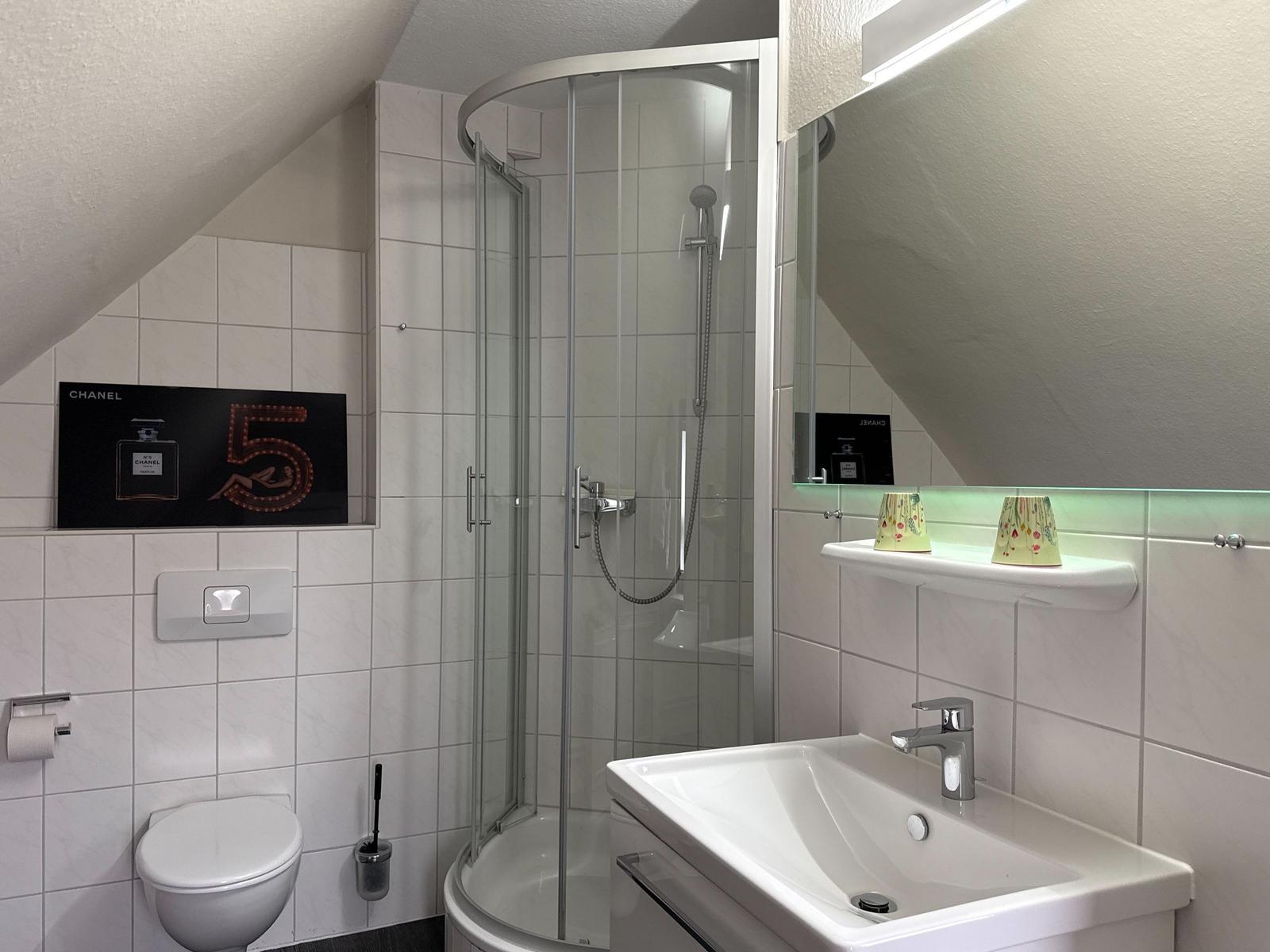 Bathroom with shower, sink, and toilet. Wall with Chanel poster.
