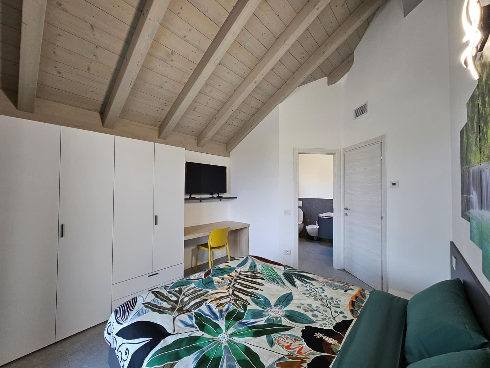 Schlafzimmer mit Bett, Kleiderschrank und Schreibtisch unter Holzdecke.